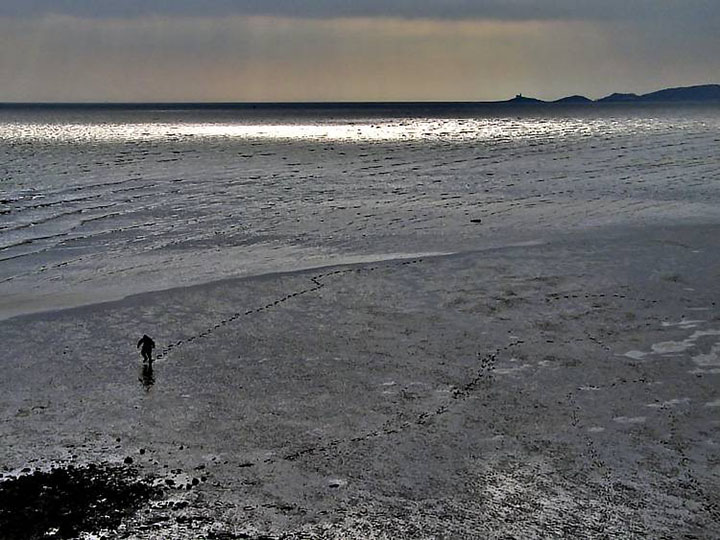 Child walking in soft sand beyond the end of the pier